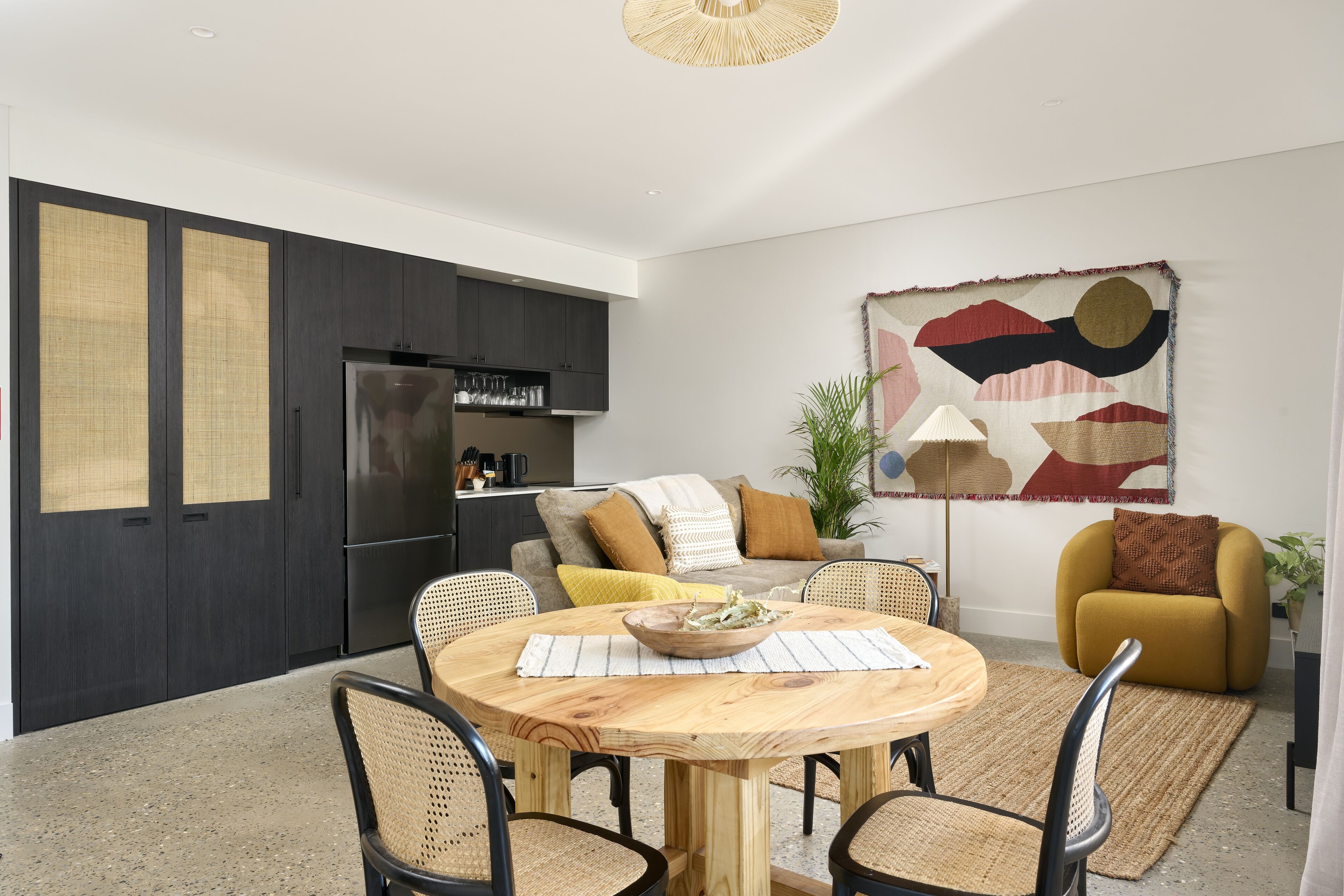 Una cocina moderna con armarios oscuros, un refrigerador y un comedor con mesa y sillas de madera.