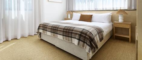 Un dormitorio ordenado con cama, mesita de noche y lámpara.