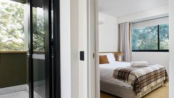 A hotel room with a bed, a window with a view of trees, and a sliding door to the outside.