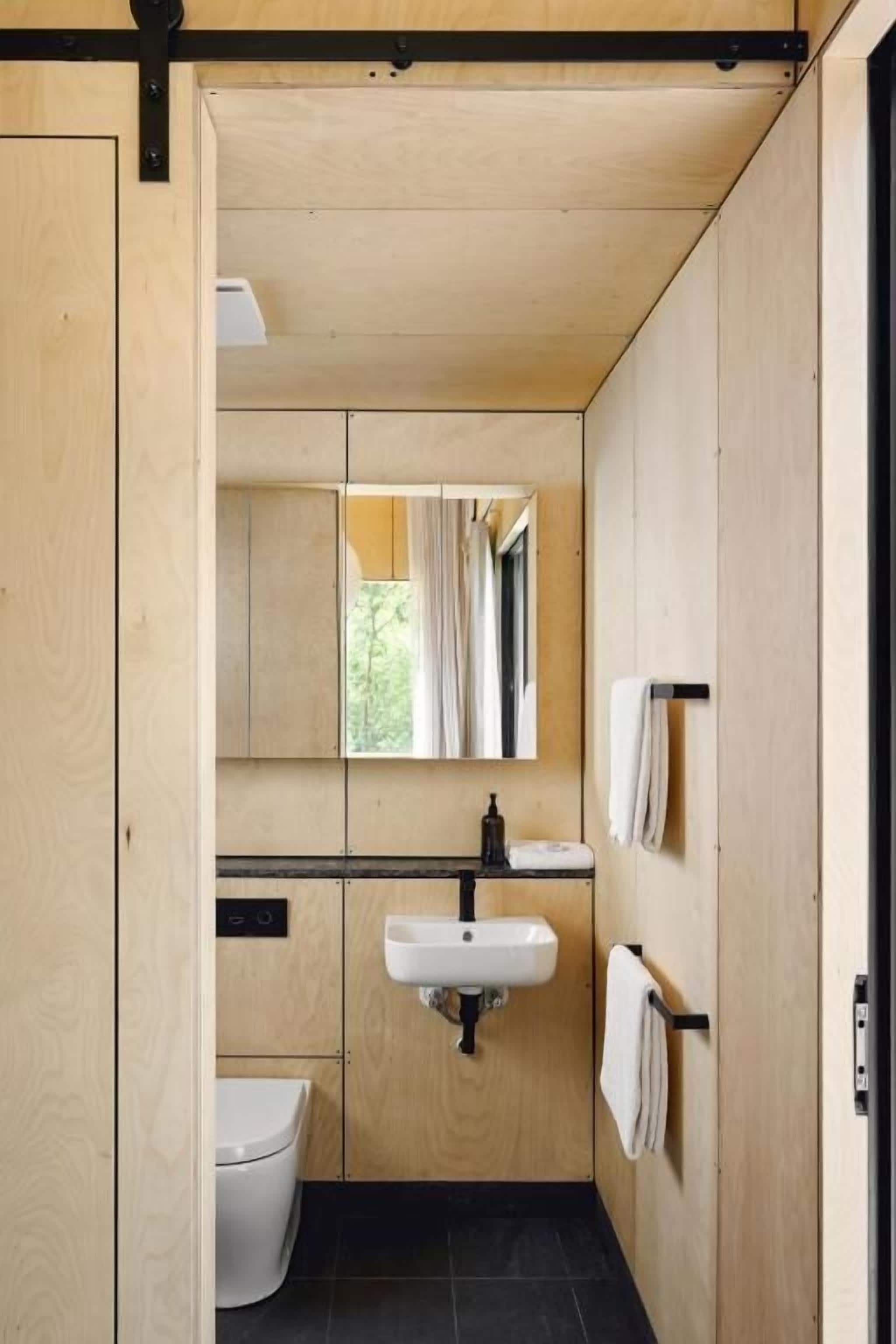 Une petite salle de bain au décor intérieur en bois, avec un lavabo blanc, un miroir et des toilettes.