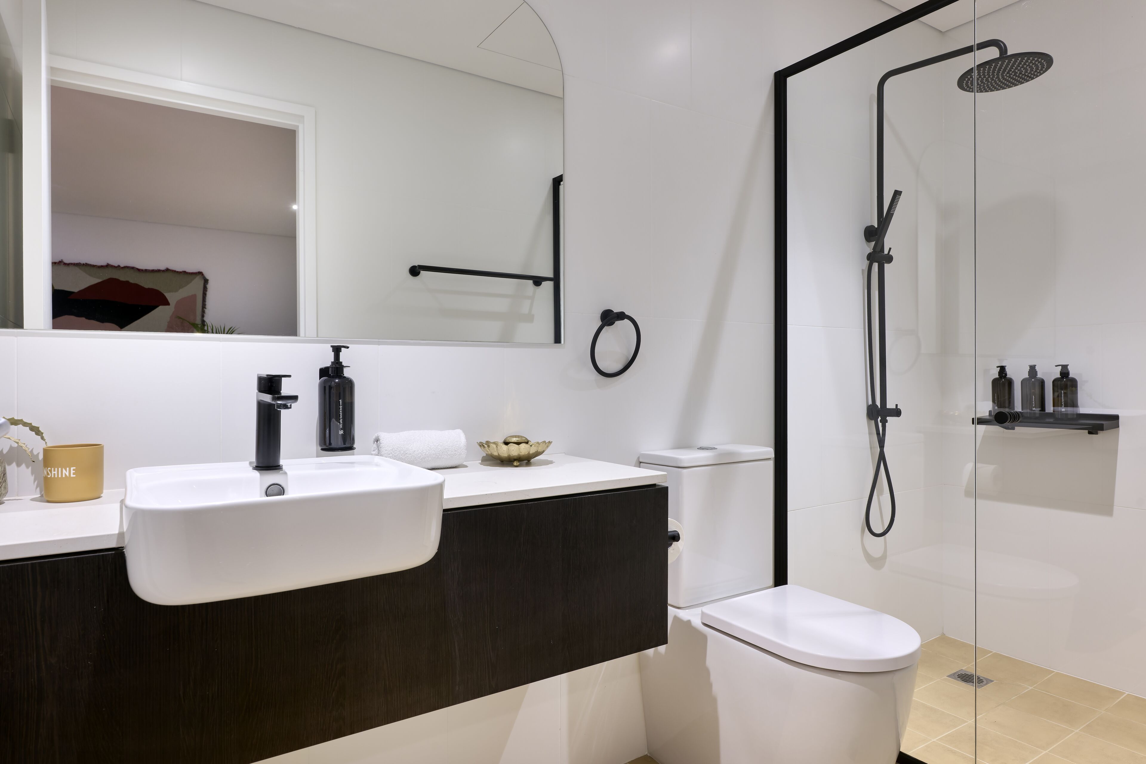 A modern bathroom with a white sink, dark vanity, and a glass-enclosed shower.