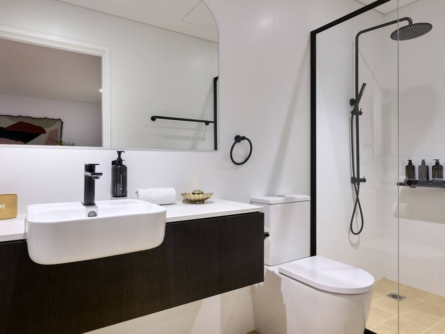 A modern bathroom with a white sink, dark vanity, and a glass-enclosed shower.