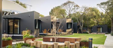A modern residential area with a house featuring large windows, a well-maintained garden with wooden planters, and a clear view of the surrounding trees.