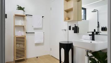 Un baño moderno con lavamanos blanco, pedestal negro, estante de madera y espejo sobre el lavamanos.