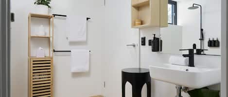 Une salle de bain moderne avec un lavabo blanc, un socle noir, une étagère en bois et un miroir au-dessus du lavabo.