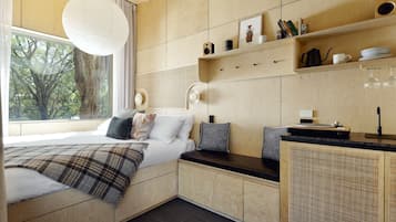 A modern bedroom with a large window, a bed with a plaid blanket, a bedside table, and a built-in wooden cabinet with shelves.
