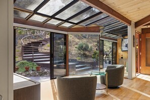 A modern interior with a glass wall, wooden staircase, and seating area. - Sea of Tranquility: Iconic Glass House in Forest Glade 3BR2BA 30Night min (Carmel)