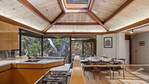 Une cuisine moderne dotée d’un îlot central, de grandes fenêtres et d’un coin repas avec une longue table.