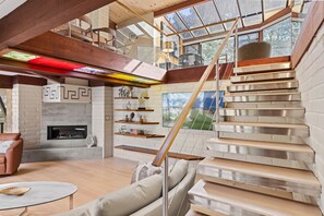 A modern interior with a staircase, fireplace, and open-plan living area. - Sea of Tranquility: Iconic Glass House in Forest Glade 3BR2BA 30Night min (Carmel)