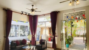 Un salon moderne avec une table basse en verre, deux canapés, un ventilateur de plafond et une vue sur l’extérieur.