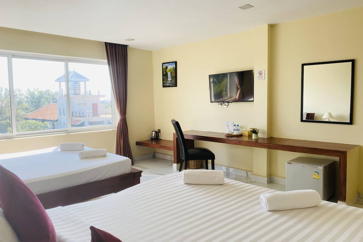 A hotel room with two beds, a desk, a TV, a mirror, and a window with a view of buildings.
