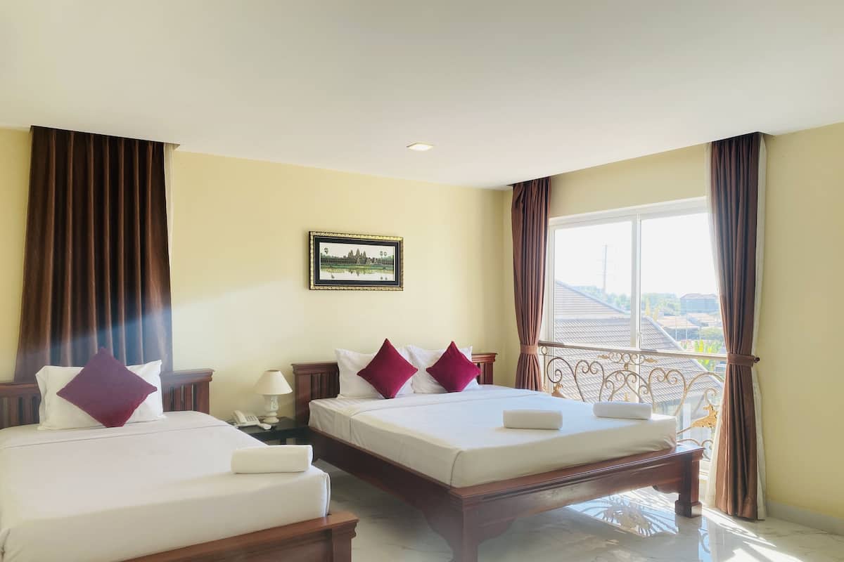 A hotel room with two beds, a nightstand with a lamp, a framed picture on the wall, and a balcony with a view of the city.