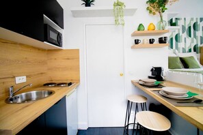 Une cuisine moderne avec un plan de travail en bois, un évier en acier inoxydable et une porte blanche. On y trouve des étagères avec des plantes et des ustensiles de cuisine, ainsi qu’un coin repas avec des tabourets.