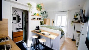 Et kompakt, moderne soveværelse med seng, sengebord og et lille siddeområde med skamler.