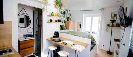 Quarto compacto e moderno com cama, mesa de cabeceira e um pequeno espaço de estar com banquinhos.