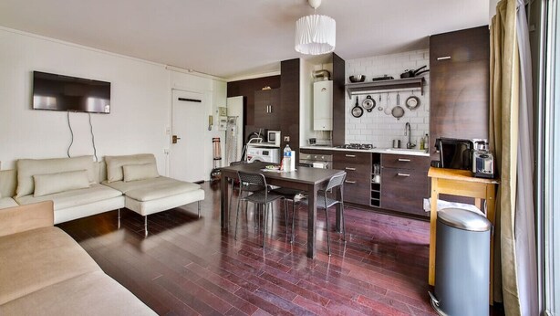 A modern living room with a sofa, dining table, and chairs. The kitchen features dark cabinetry, a stove, and hanging pots. - Appart 4pers#St Antoine#Bastille#Nation (Paris)