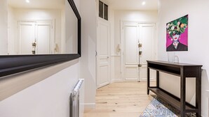 A hallway with white doors, a black-framed mirror, a tiled floor, and a colorful rug. - Au cœur des Batignolles (Paris)