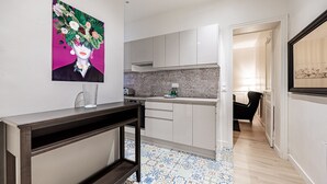A modern kitchen with white cabinets, a tiled backsplash, and a dining area with a black chair. - Au cœur des Batignolles (Paris)