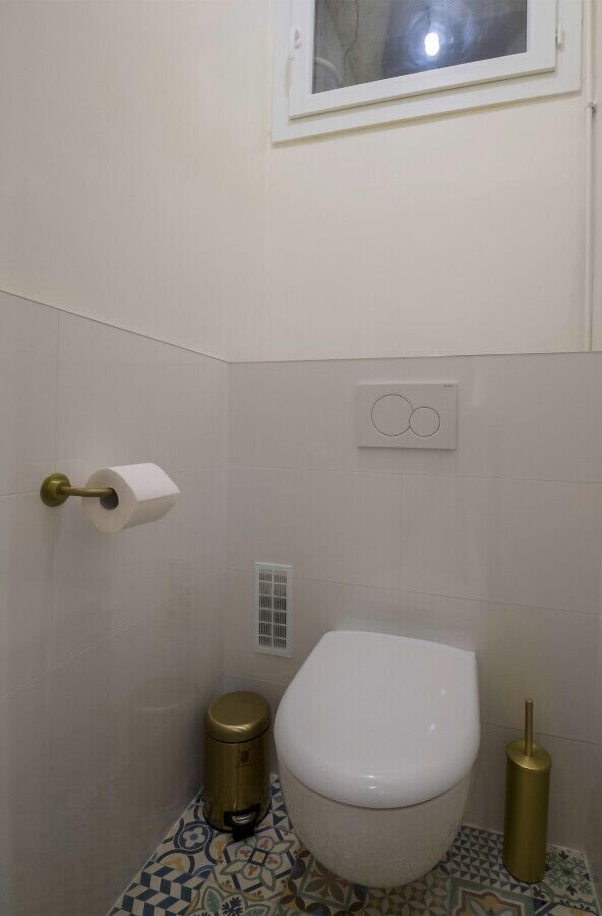 Une salle de bain équipée de toilettes, d’un porte-rouleau de papier toilette, d’une poubelle et d’un bidet.