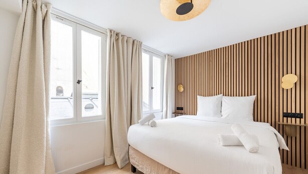 A modern hotel room with a large bed, wooden panel wall, and a view through the window. - 1 Bedroom#4 pers#Mouffetard#Port-Royal#La Sorbonne (Paris)