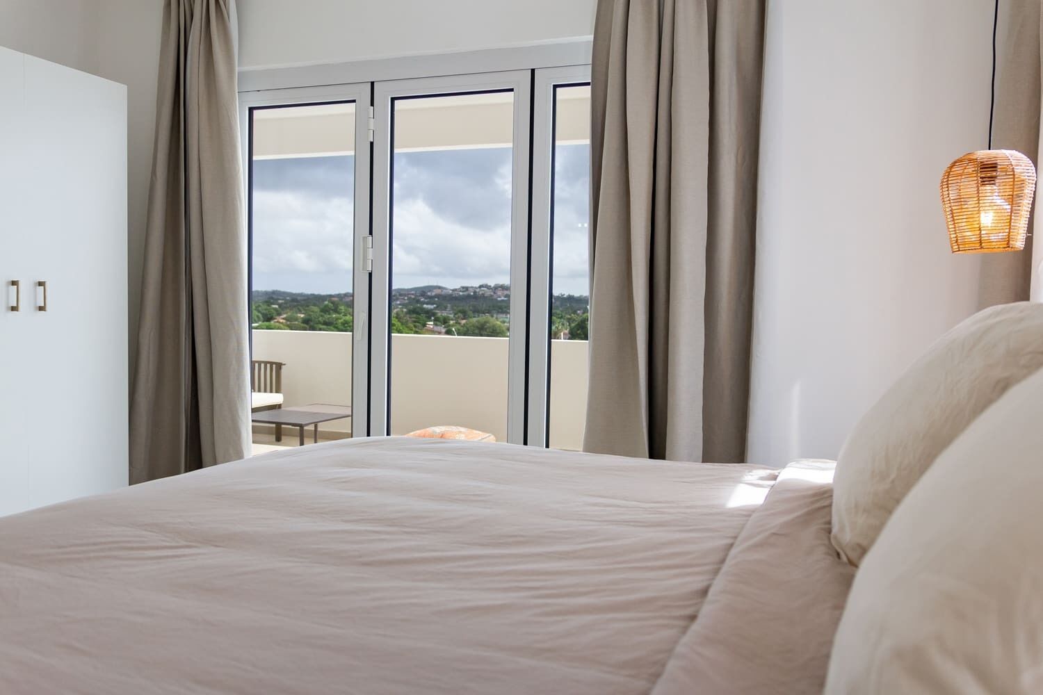 Un dormitorio con una cama grande, vistas al exterior a través de un ventanal corredero y una lámpara de mimbre.
