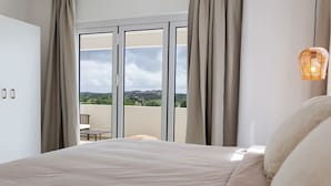 Un dormitorio con una cama grande, vistas al exterior a través de un ventanal corredero y una lámpara de mimbre.