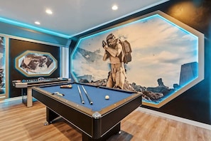 Una mesa de billar en una habitación con un gran mural de una figura con temática espacial y una nave espacial.