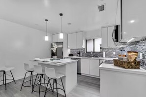 A modern kitchen with white cabinetry, a central island with bar stools, a built-in oven, and a backsplash of gray tiles.