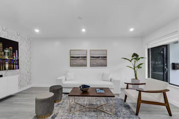 A modern living room with a white sofa, a coffee table, and a TV mounted on a marble wall.