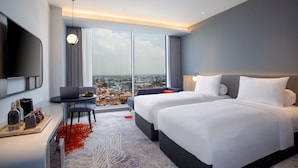 A modern hotel room with a large bed, a desk with a laptop, and a city view through large windows. - Harris Hotel & Convention Cibinong City Mall Bogor (Cibinong)
