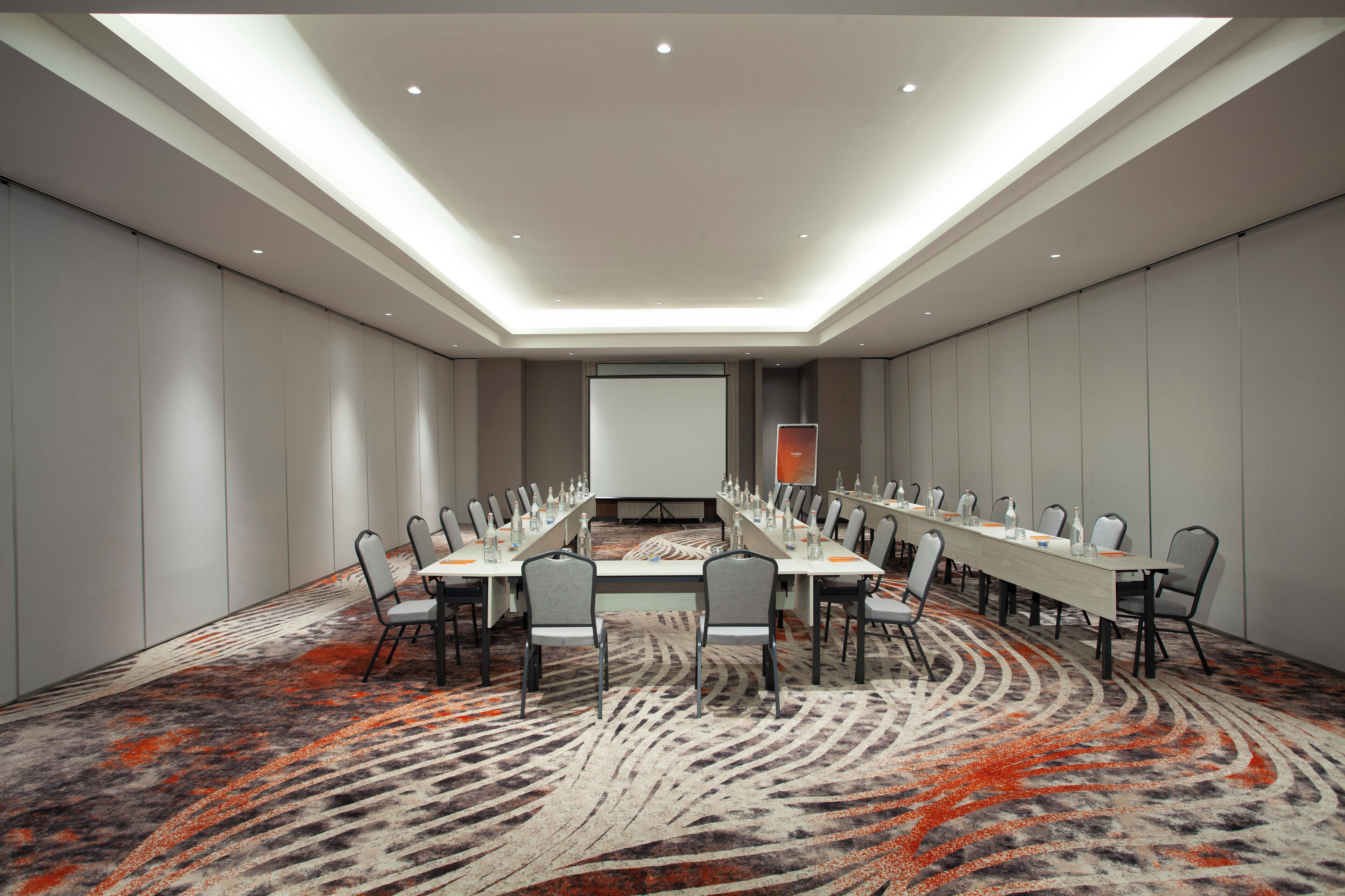A conference room with a long table, chairs, and a projector screen.