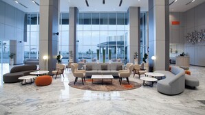 A spacious lobby with a modern design, featuring a central seating area with sofas and armchairs, a marble floor, and large windows offering a view of the building and the cityscape. - Harris Hotel & Convention Cibinong City Mall Bogor (Cibinong)