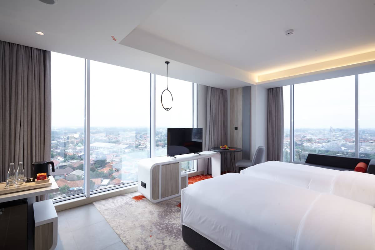 Une chambre d’hôtel moderne dotée d’un grand lit, d’un bureau avec une télévision et offrant une vue sur la ville grâce à de grandes fenêtres.