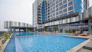 A modern hotel with a large outdoor swimming pool, sun loungers, and a view of the city skyline. - Harris Hotel & Convention Cibinong City Mall Bogor (Cibinong)