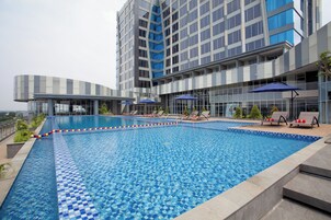 Un hotel moderno con una gran piscina al aire libre, tumbonas y vistas al horizonte de la ciudad.