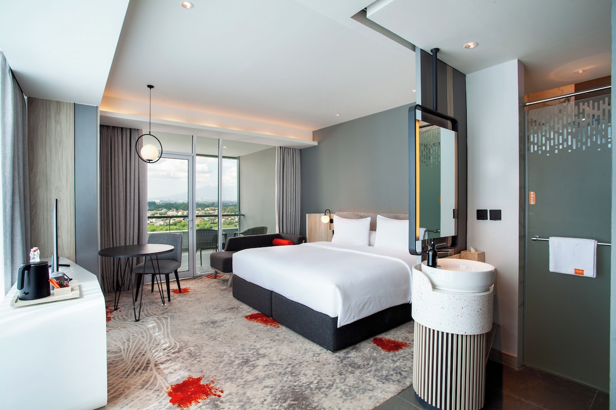 A modern hotel room with a large bed, a desk, and a bathroom.