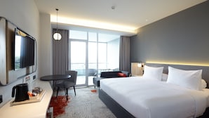 A modern hotel room with a large bed, a desk with a coffee maker, a TV, and a balcony with a view. - Harris Hotel & Convention Cibinong City Mall Bogor (Cibinong)