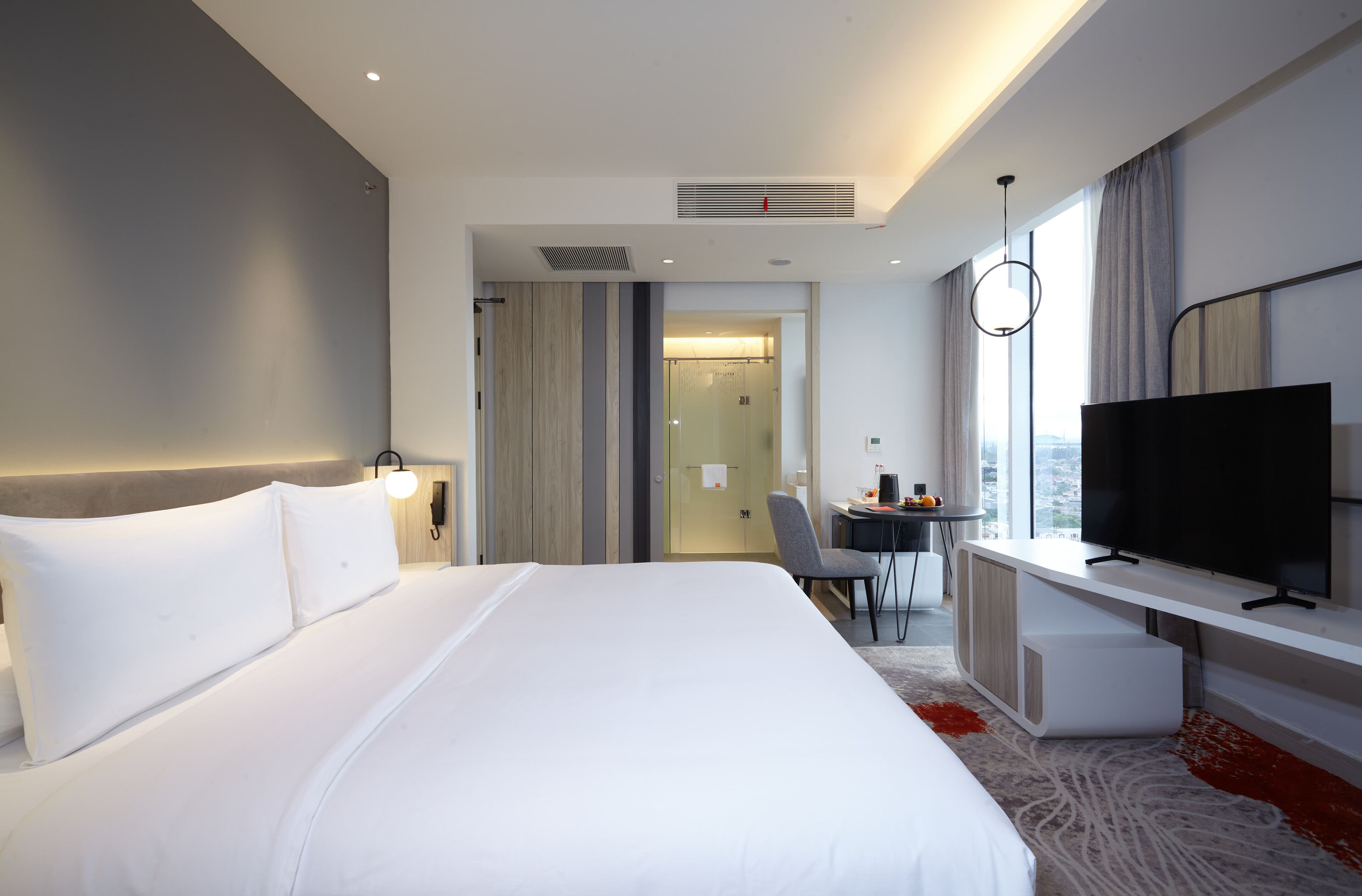 Ein modernes Hotelzimmer mit einem großen Bett, einem Schreibtisch, einem Fernseher und Blick auf die Stadt.