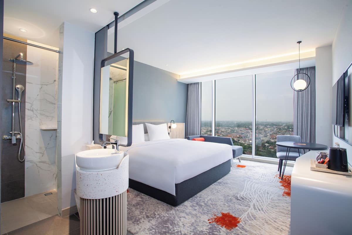 Une chambre d’hôtel moderne dotée d’un grand lit, d’une salle de bain avec douche, d’un lavabo et offrant une vue sur la ville.