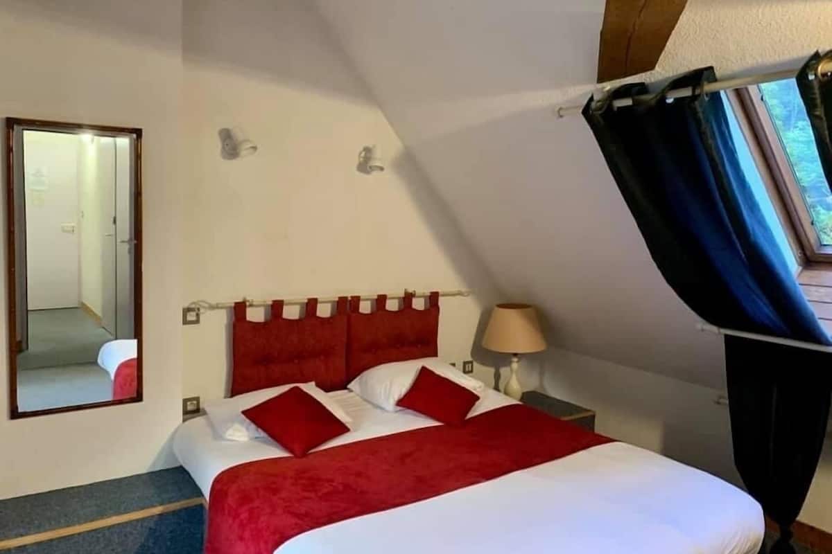 Une chambre à coucher avec un lit, un miroir, une table de chevet et une fenêtre avec des rideaux.