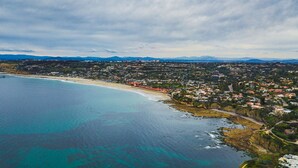 An aerial view of a coastal town with a beach, residential areas, and a bridge.