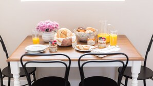 A breakfast table with a variety of food items, including pastries, a fruit bowl, and a pitcher of orange juice.