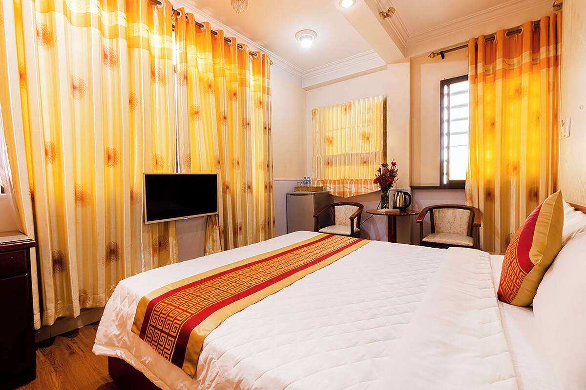 Ein Hotelzimmer mit einem großen Bett, einem Fernseher, einem Schreibtisch mit Stuhl und Vorhängen.