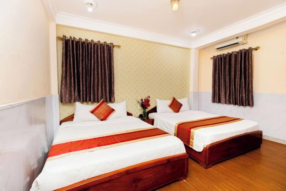 A hotel room with two single beds, wooden flooring, and a wall-mounted air conditioner.
