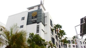 Un moderno edificio de hotel con un logotipo destacado, múltiples ventanas y palmeras circundantes.