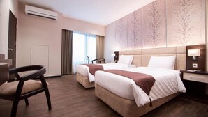 Habitación de hotel con dos camas, un escritorio, una silla y un ventanal con cortinas.