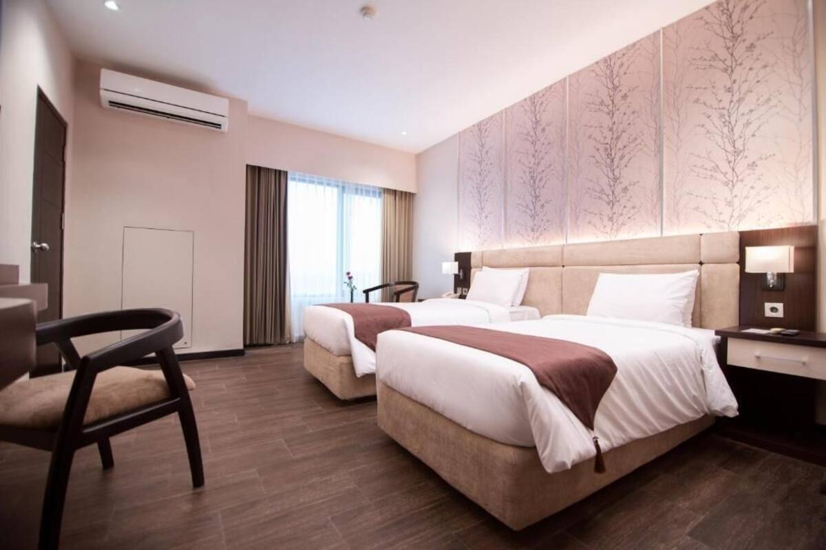 A hotel room with two beds, a desk, a chair, and a large window with curtains.