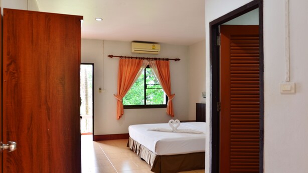 A hotel room with a bed, a window with curtains, and an air conditioning unit. - Heimat Garden (Ko Yao)