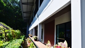 A covered corridor with potted plants along the sides, a wooden bench, and a pathway leading to a building entrance. - Heimat Garden (Ko Yao)