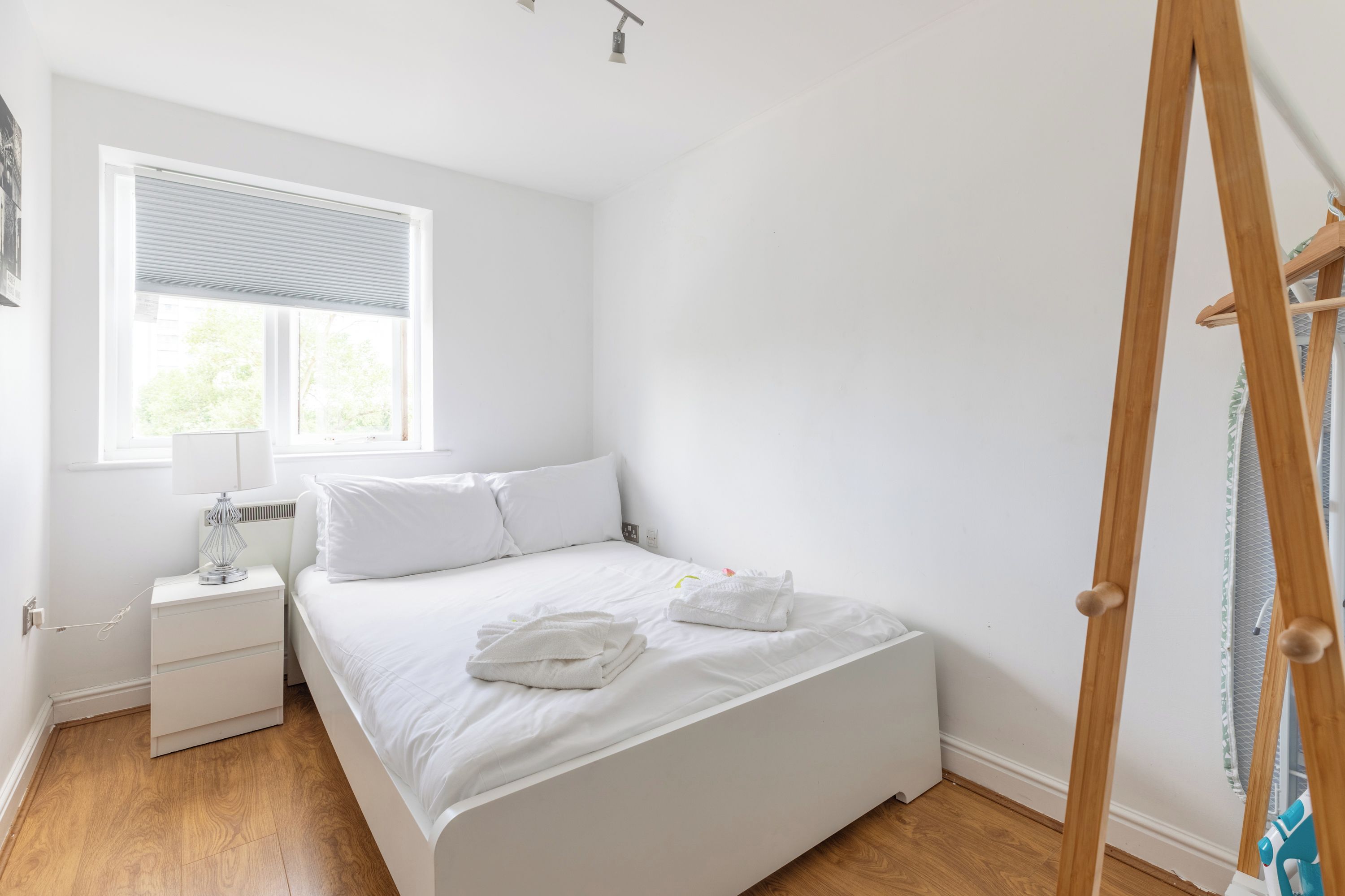 A minimalist bedroom with a single bed, a bedside table, a lamp, and a window with blinds.